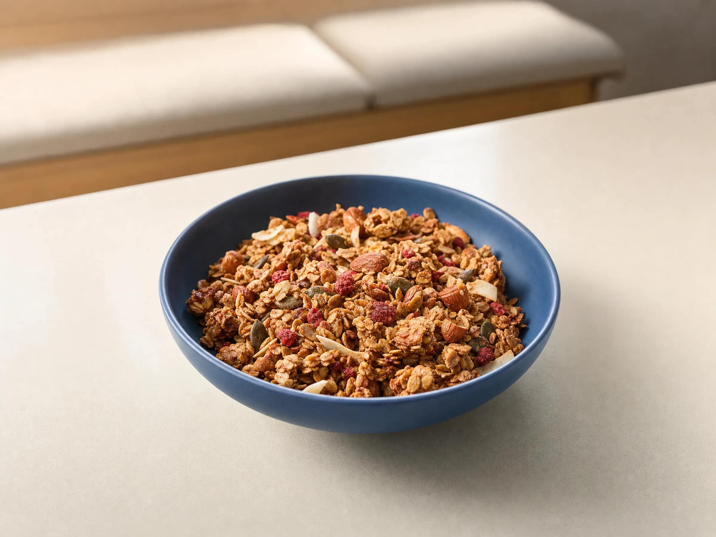 Granola-Cluster in blauer Schüssel Hellgoldene Granola-Cluster mit Nüssen, Kernen, Kokoschips und roten Fruchtstücken in einer blauen Schüssel