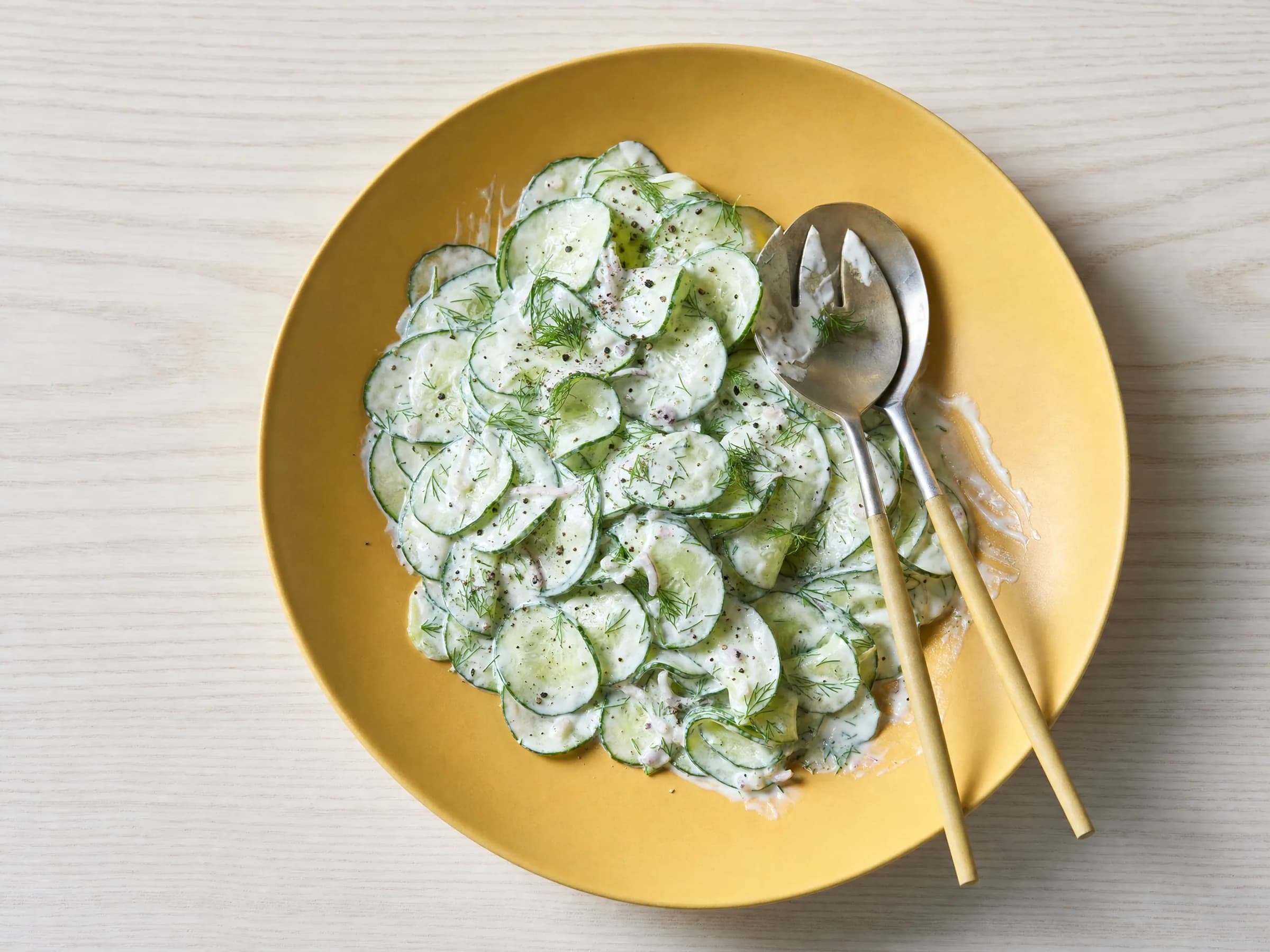 Gurkensalat mit Joghurt-Dill-Dressing – Rezeptfoto Cremiger Gurkensalat mit Dill und Pfeffer auf gelber Platte